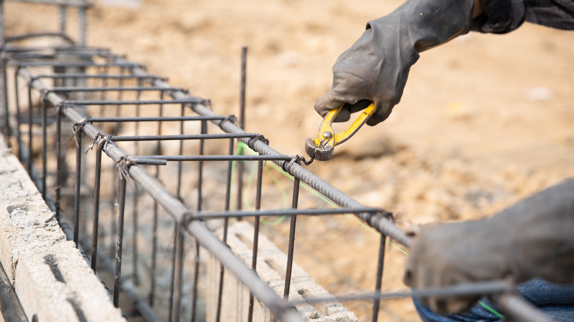 Worker tying steel rebar with yellow pliers at a construction site