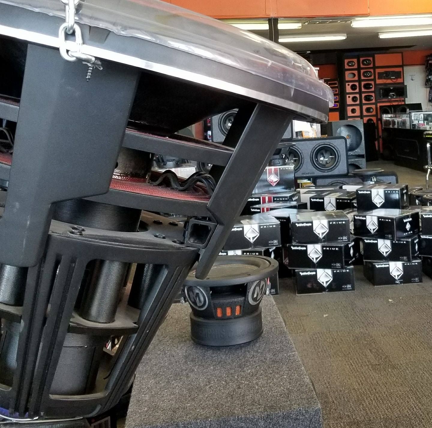 Close-up of a large subwoofer in a car audio store. Black and silver speakers on display in a retail setting.