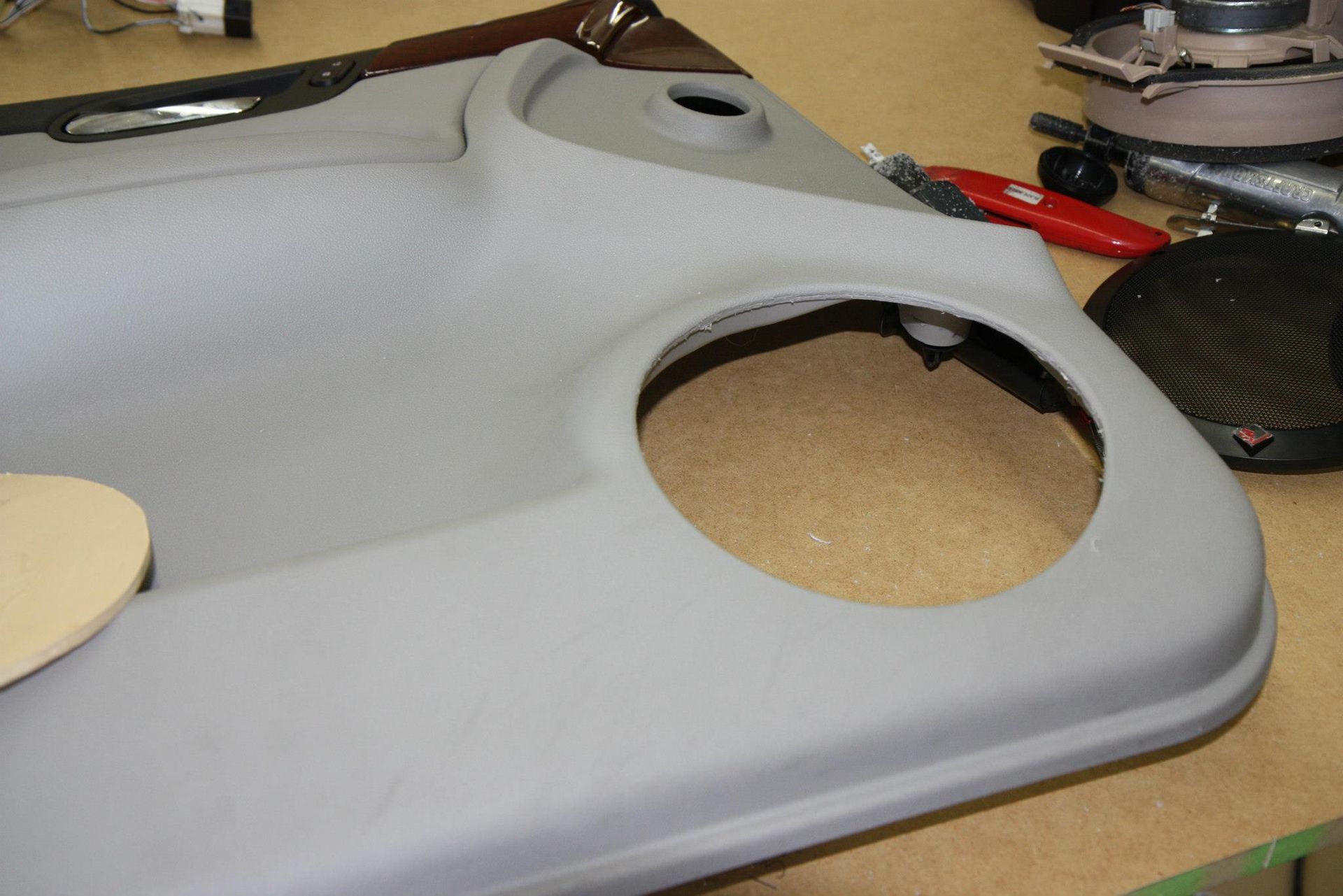 Gray car door panel with a large speaker hole.