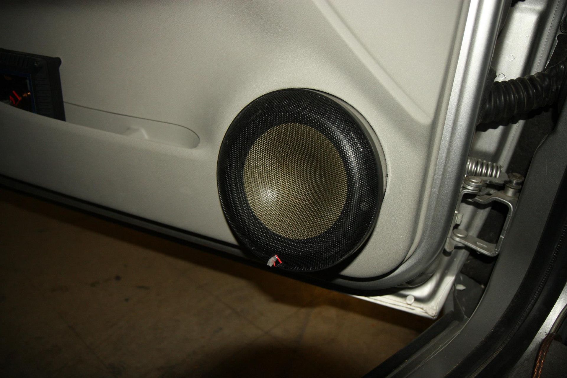 Car door panel with round speaker. Black mesh speaker grill set into light gray door.