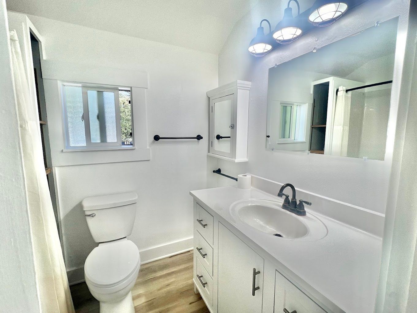 A bathroom with a toilet , sink , mirror and window.
