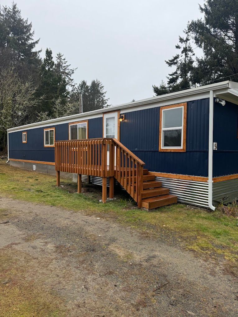 A blue mobile home with a wooden deck and stairs.