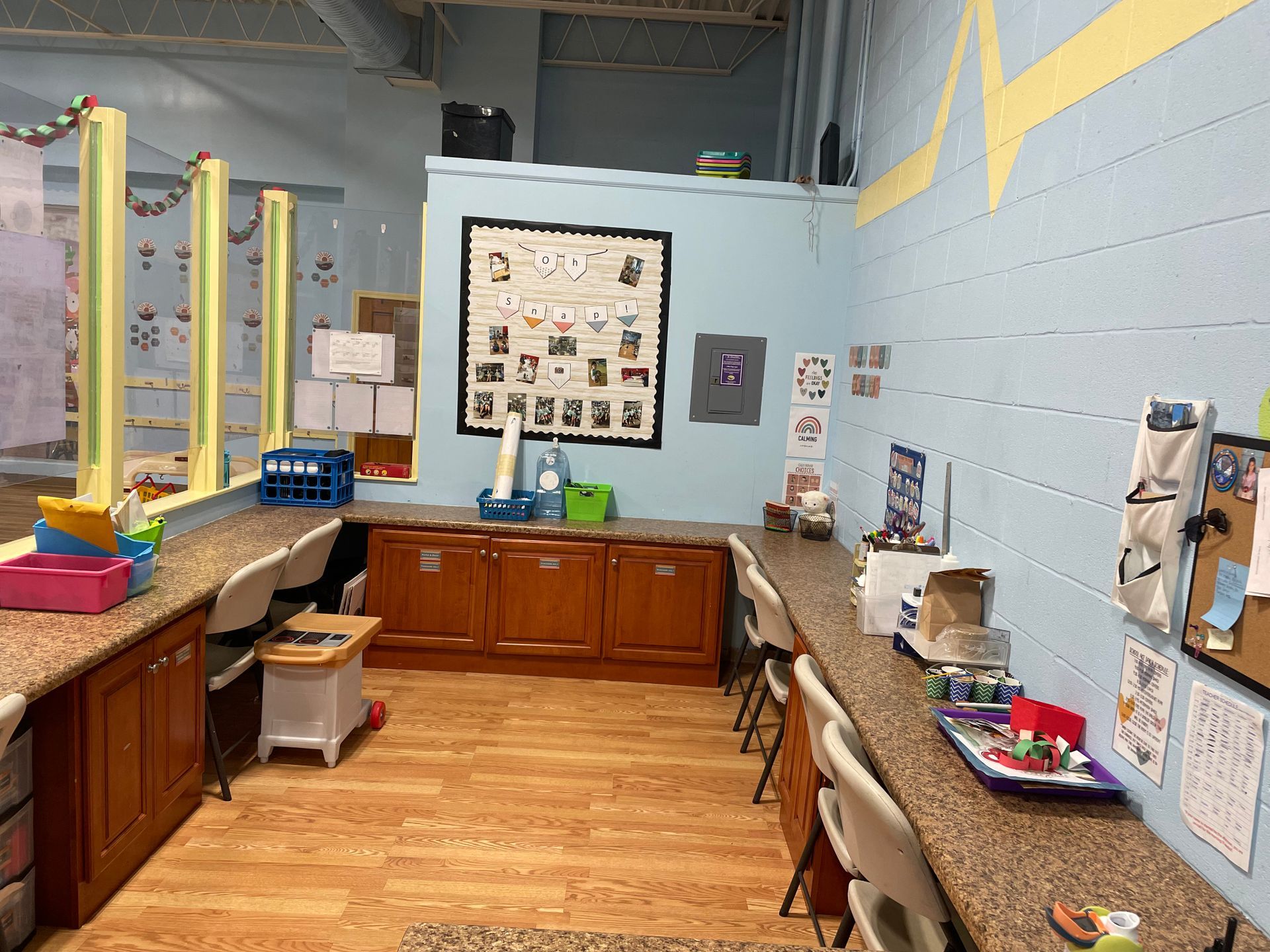 Empty classroom with wood cabinets, granite counters, and colorful wall displays under bright lights.