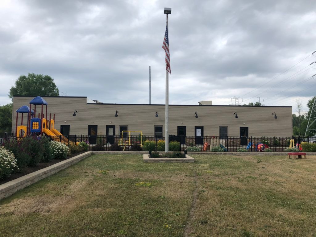 Childcare building with playground, flagpole, and cloudy sky
