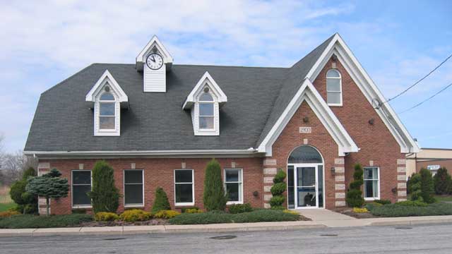 Brick childcare building with gray roof, white trim, arched entrance, and dormer windows by the road