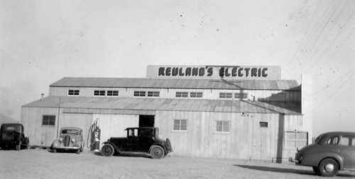 A black and white photo of a building with cars parked in front of it.