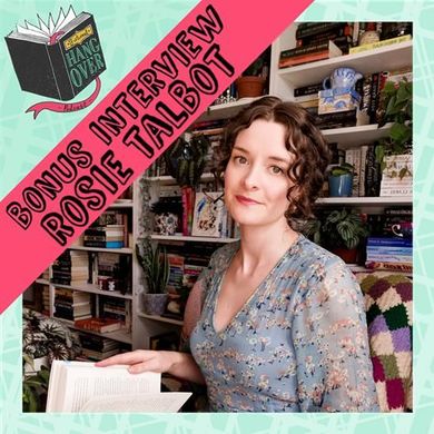 A woman is sitting in front of a bookshelf holding a book.