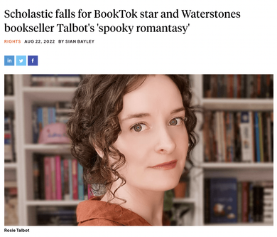 A woman with curly hair is standing in front of a bookshelf.