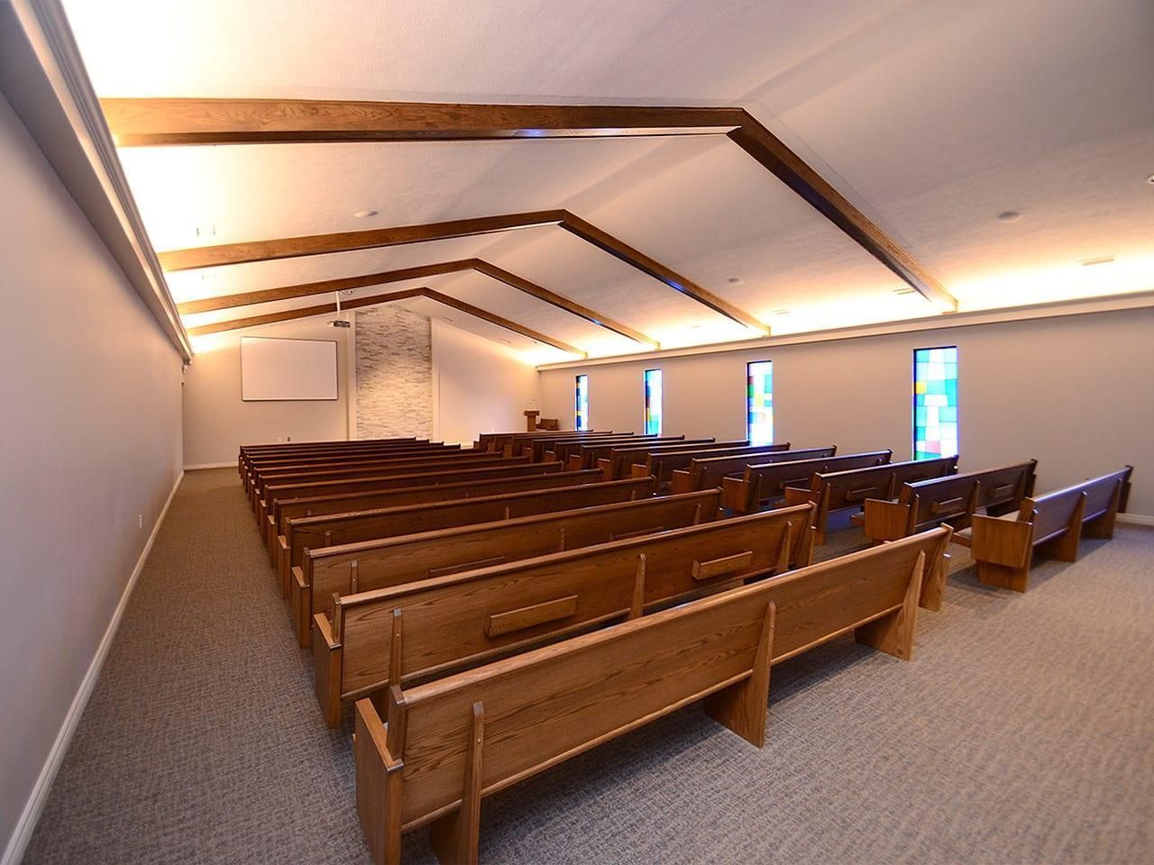 Empty church sanctuary with wooden pews, slanted ceiling beams, and stained-glass windows