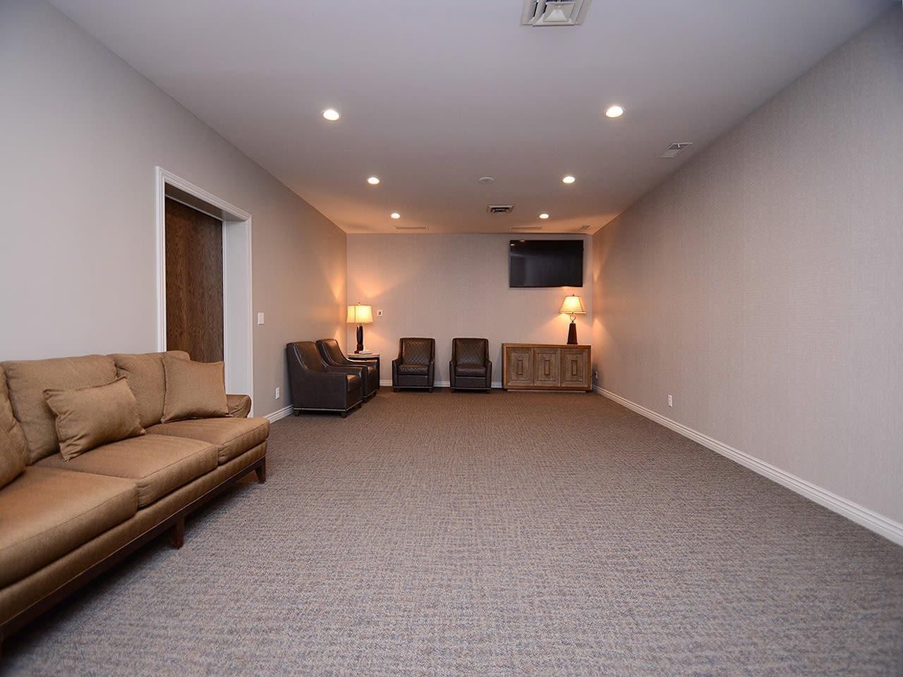 Spacious beige living room with a brown sofa, chairs, carpet, and wall-mounted TV.
