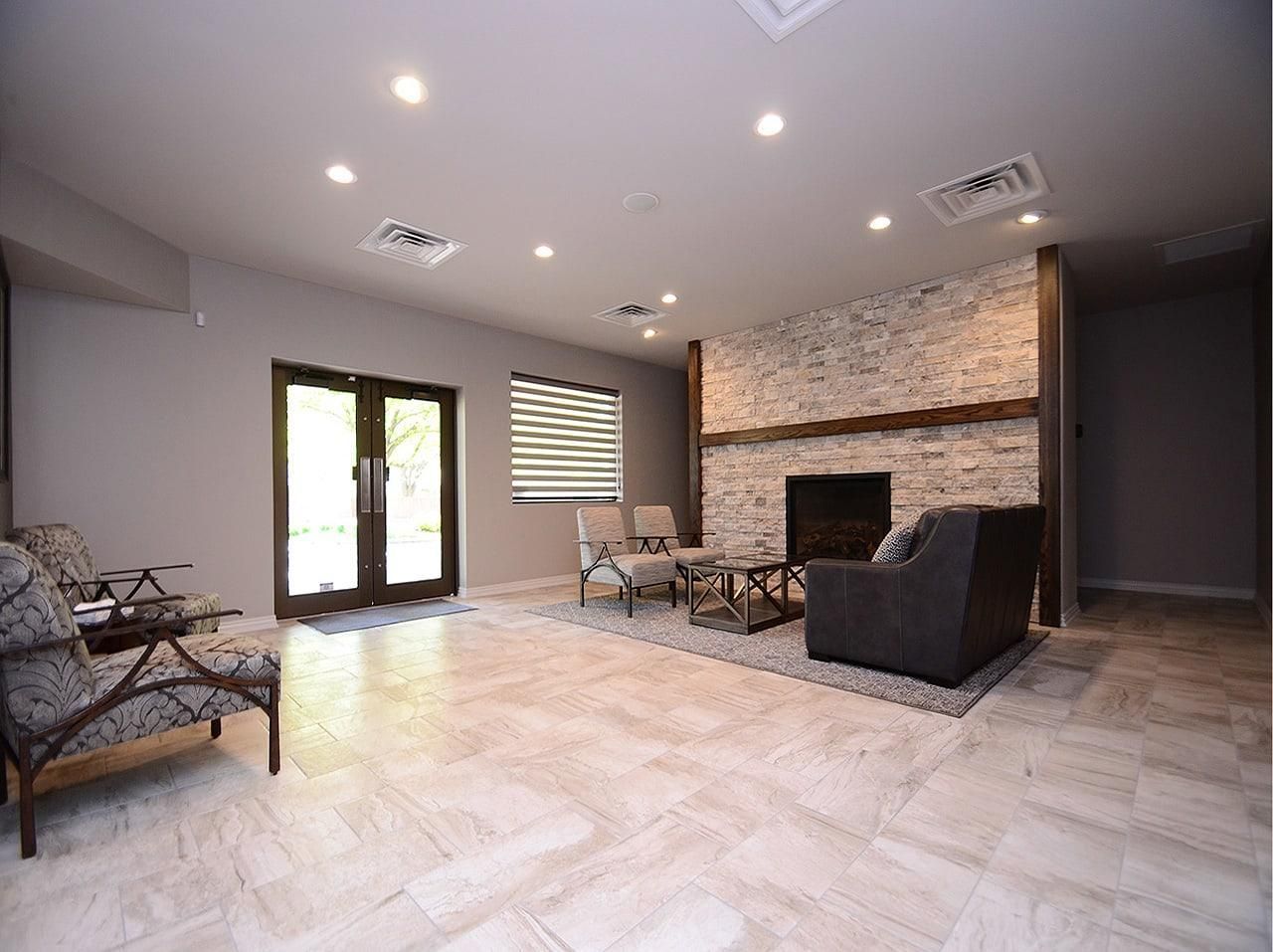 Modern living room with stone fireplace, leather chairs, tiled floor, and large windows