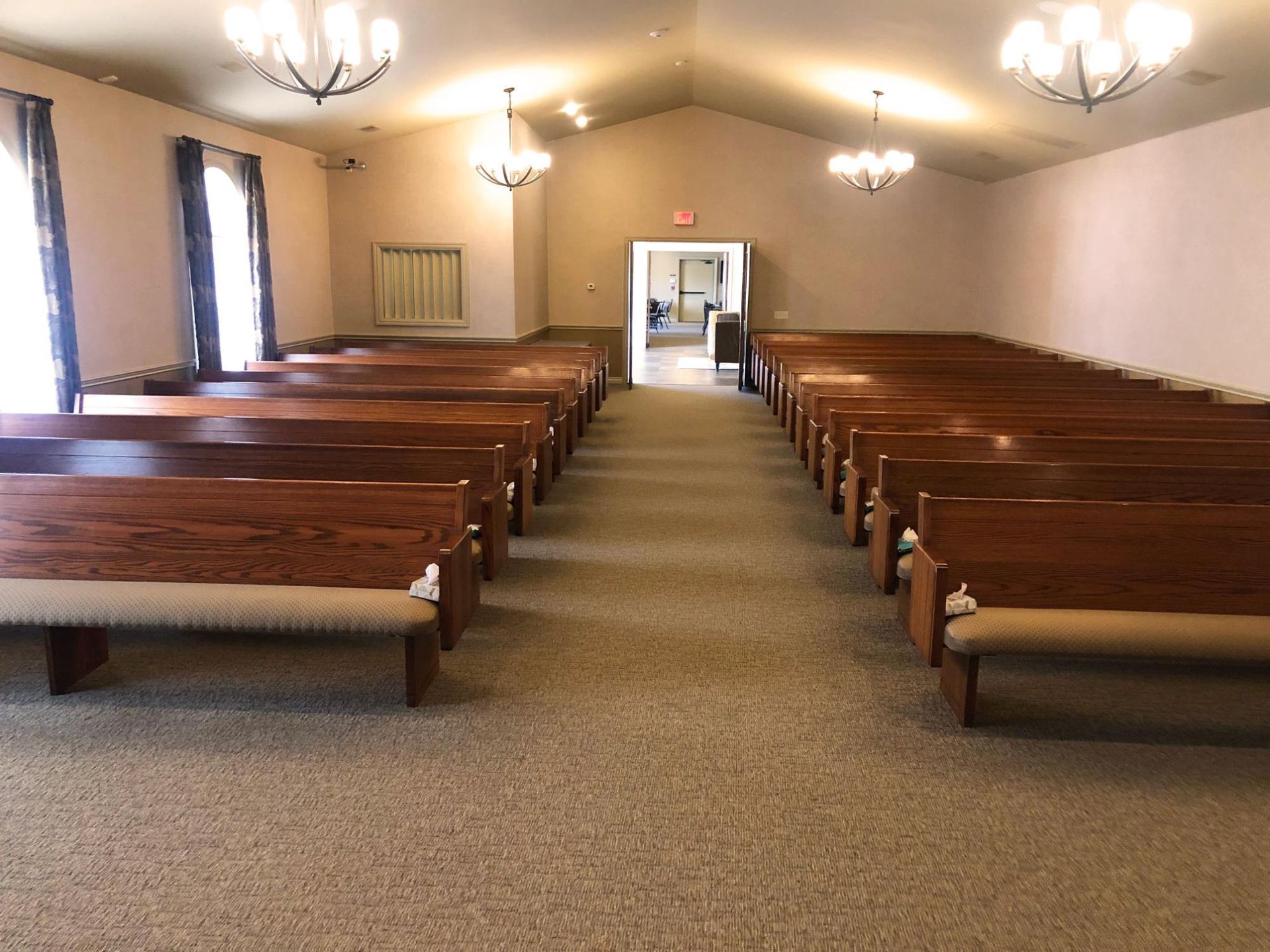 Empty church chapel with rows of wooden pews facing a central aisle and doorway.