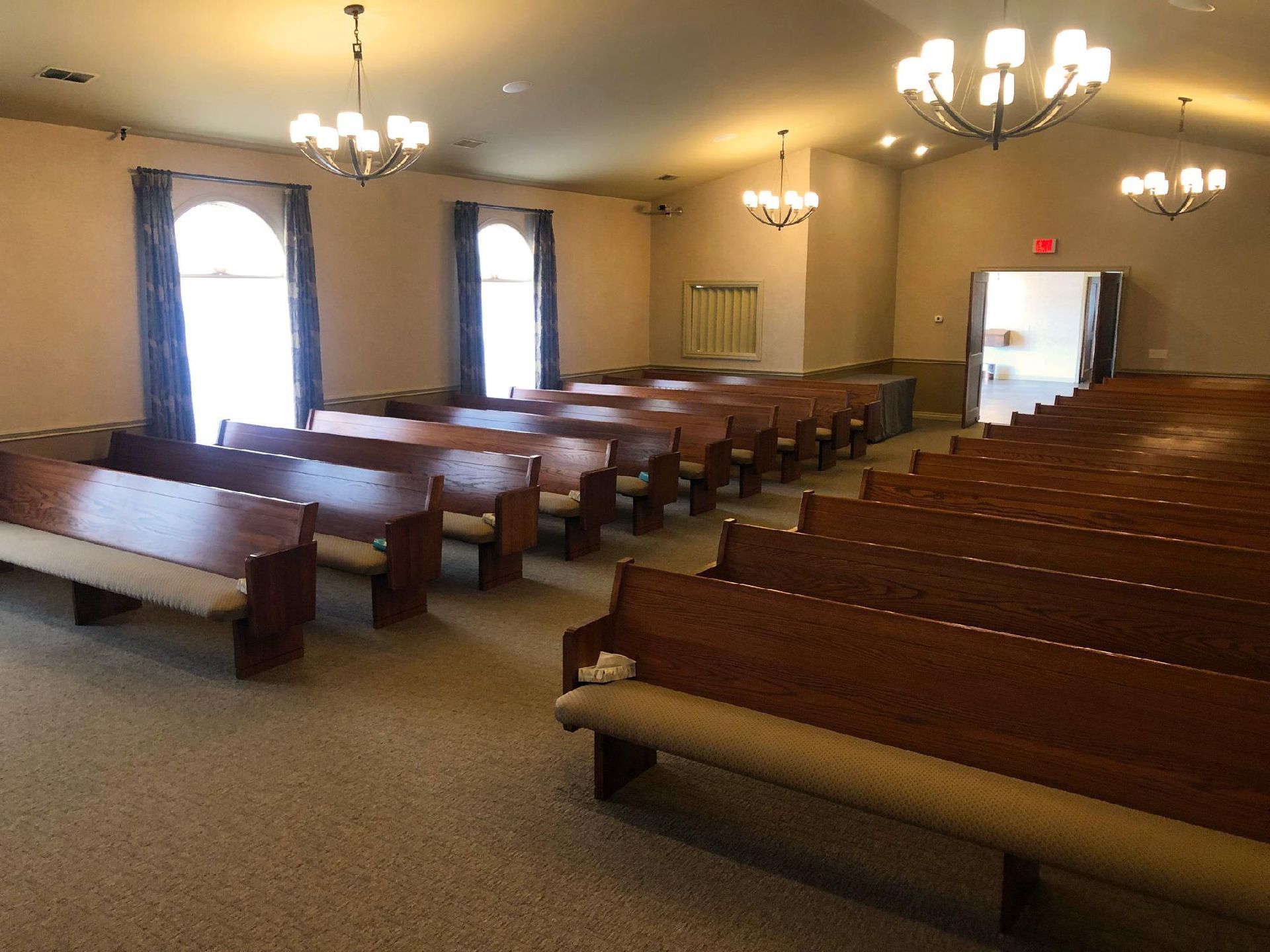 Empty church sanctuary with wooden pews, arched windows, and chandeliers