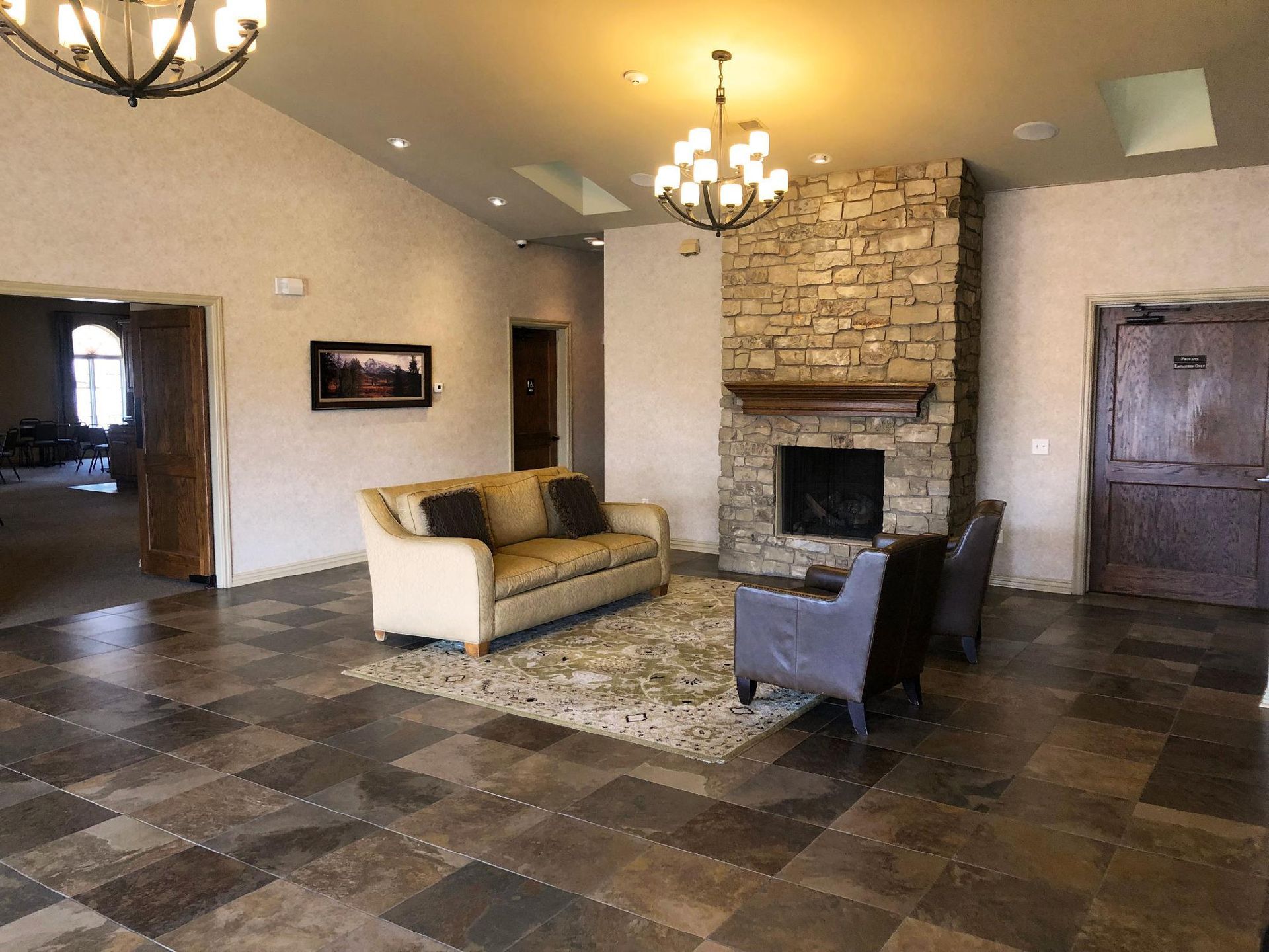 Spacious lobby with stone fireplace, chandeliers, sofa, and tiled floor