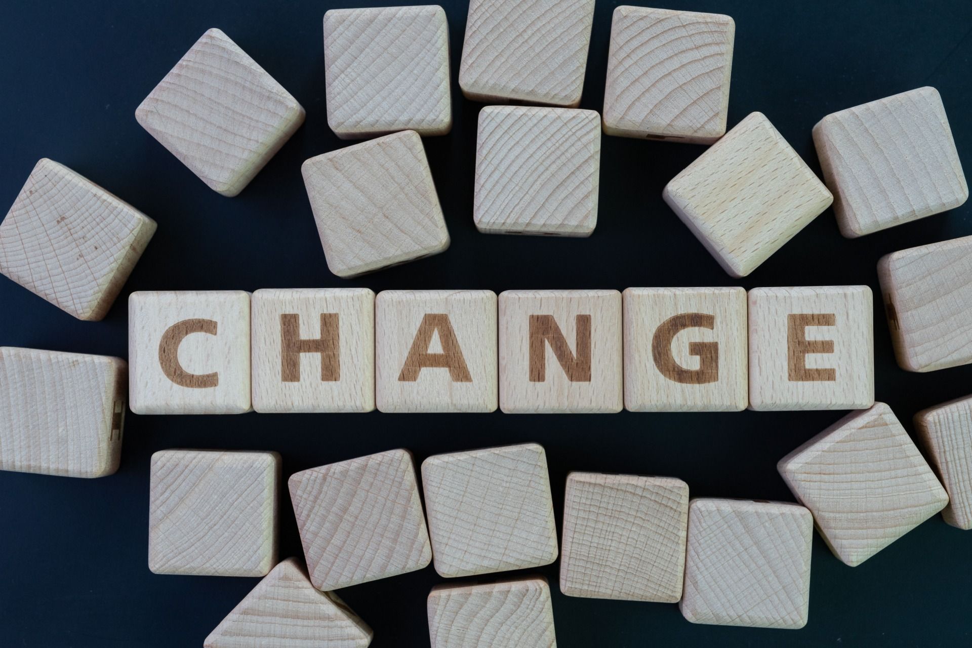 Wooden letter blocks spelling “CHANGE” surrounded by scattered white tiles on a dark background