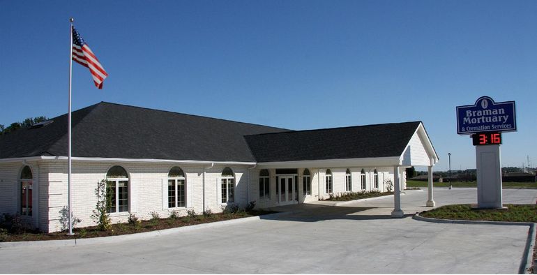 White building with American flag and a roadside sign under a clear blue sky.