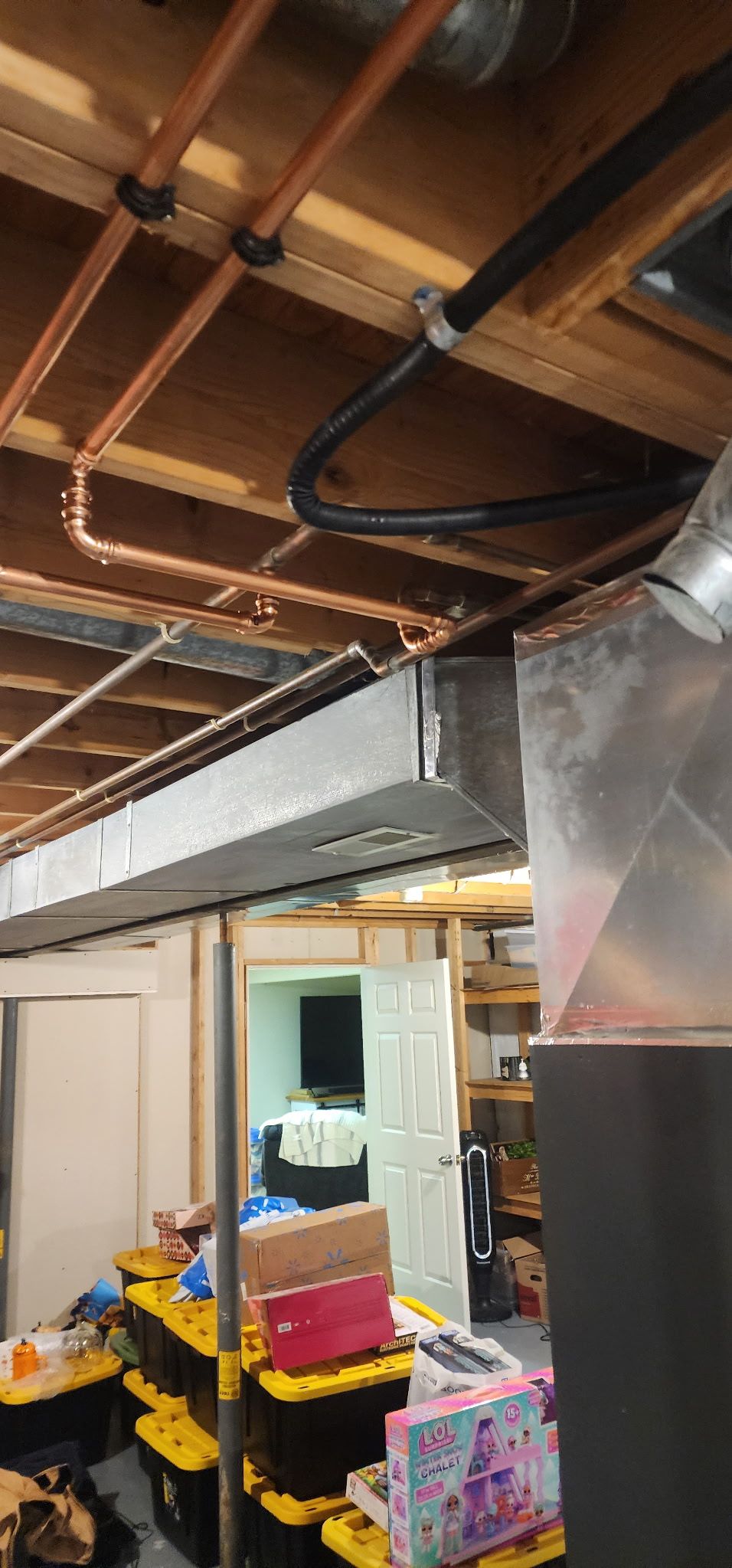Unfinished basement ceiling with exposed copper plumbing, a metal HVAC duct, and stacked storage bins in the background.