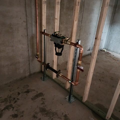 Copper plumbing assembly with a water filtration system mounted on metal support posts in an unfinished basement.