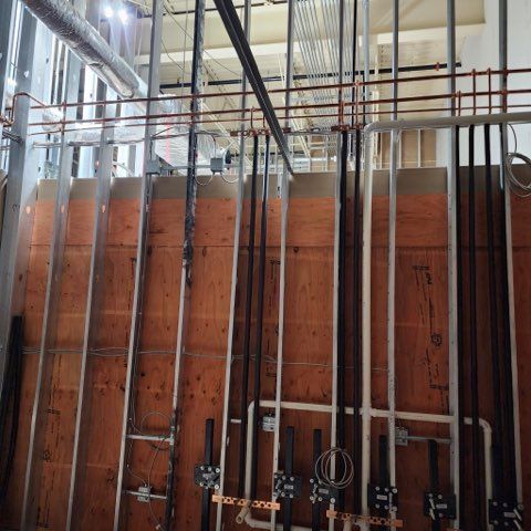 Construction site with vertical metal wall studs, plywood backing, and various copper and black pipes installed.