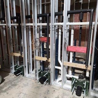 Wall-mounted toilet carrier frames and plumbing pipes installed within metal stud framing in an unfinished interior space.