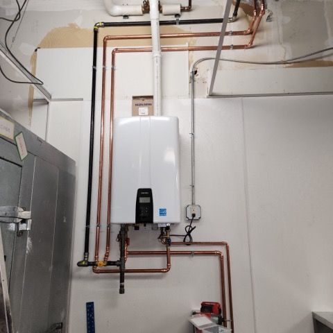 Wall-mounted white tankless water heater with copper plumbing, black gas line, and vertical vent pipe on a white wall.
