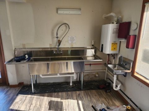 A commercial three-compartment sink and a smaller hand-washing sink installed in a room with a wall-mounted water heater.