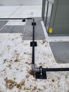 A black pipe with silver fittings runs along a snowy rooftop, supported by several black mounting blocks.