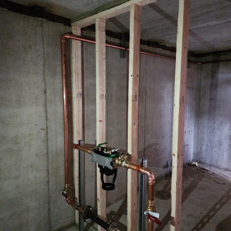 Copper plumbing pipes and a valve assembly installed within a wooden wall frame in an unfinished concrete basement.