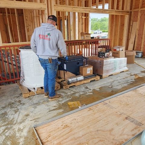 A construction worker wearing a gray hoodie stands on a concrete floor next to pallets of building materials.