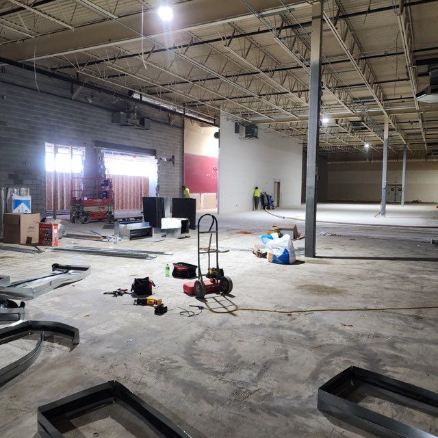 Construction site in a large, open commercial space with tools, metal materials, and workers in the background.