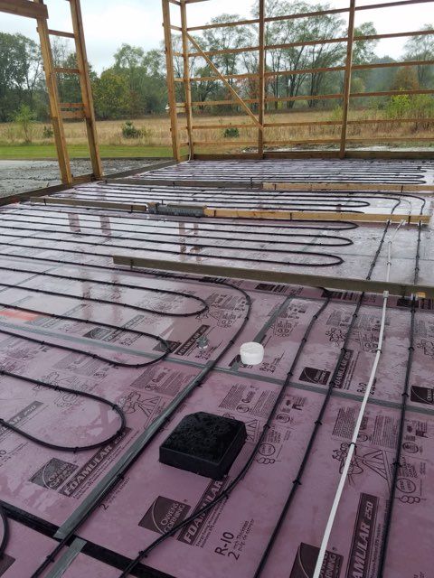 Radiant floor heating tubing installed over pink R-10 foam insulation boards inside a wooden building frame.