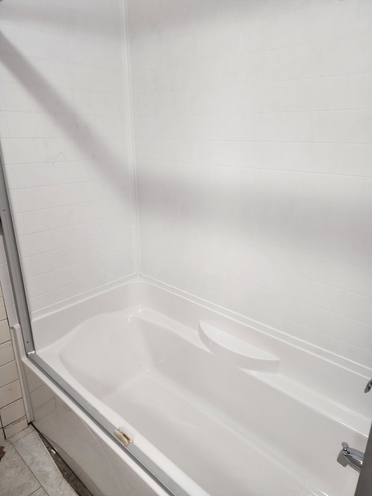 A white bathtub with an integrated shower wall and a glass enclosure frame in a tiled bathroom.