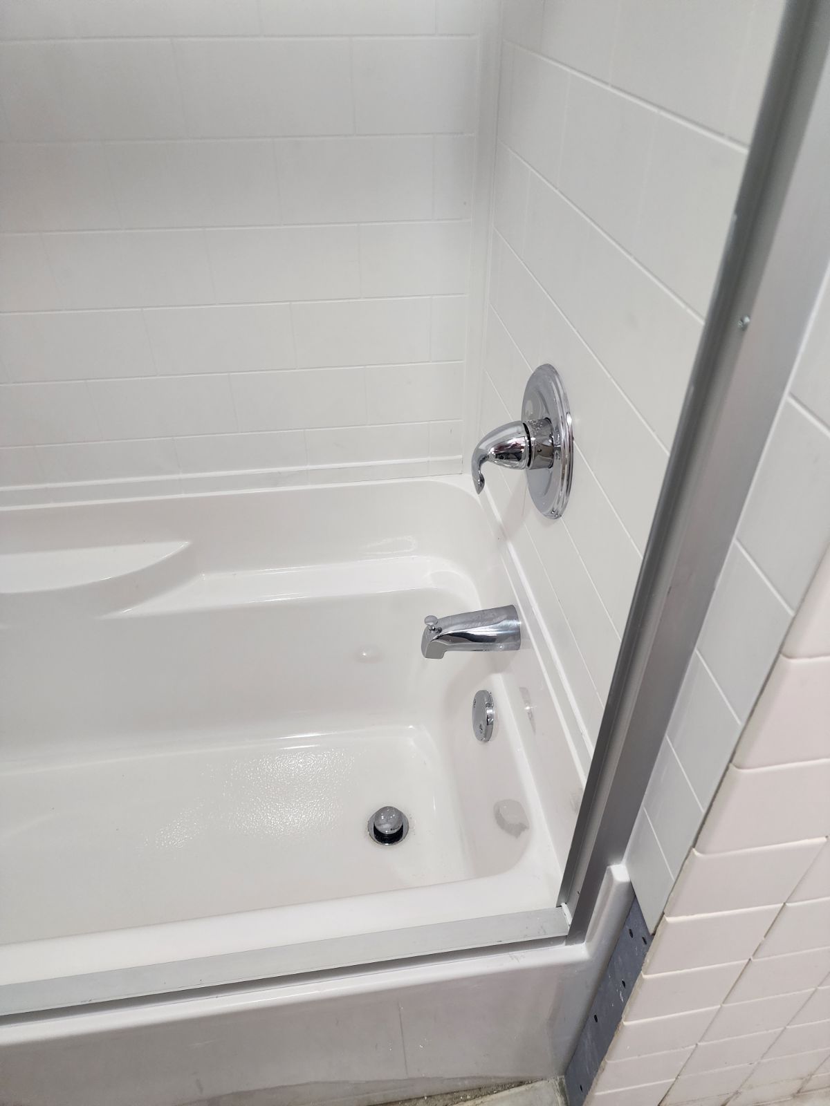 A white bathtub and shower surround with chrome fixtures, including a handle, a spout, and a drain.
