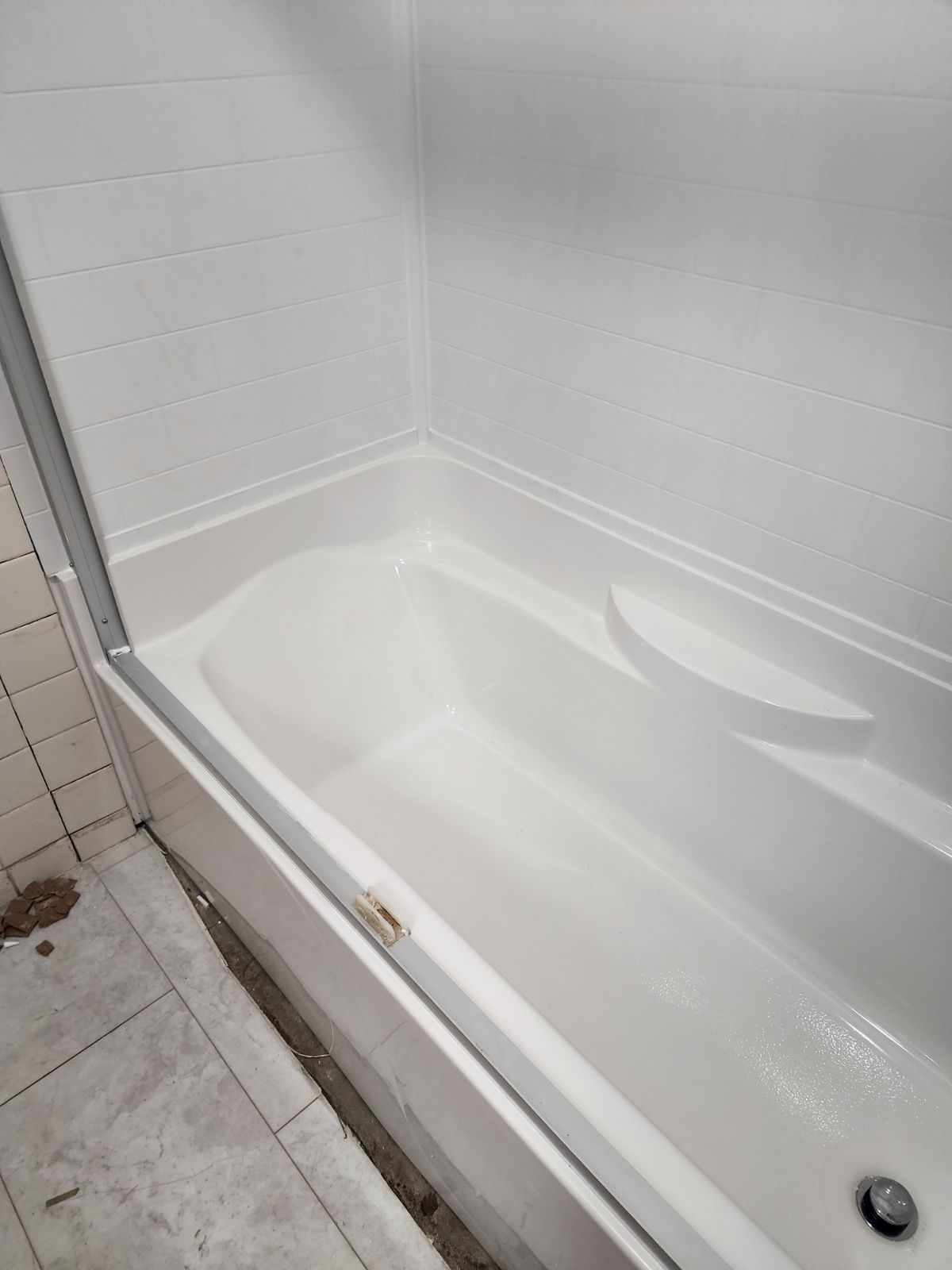 A white bathtub with a surrounding shower wall and partial frame, situated next to tiled flooring in a bathroom.