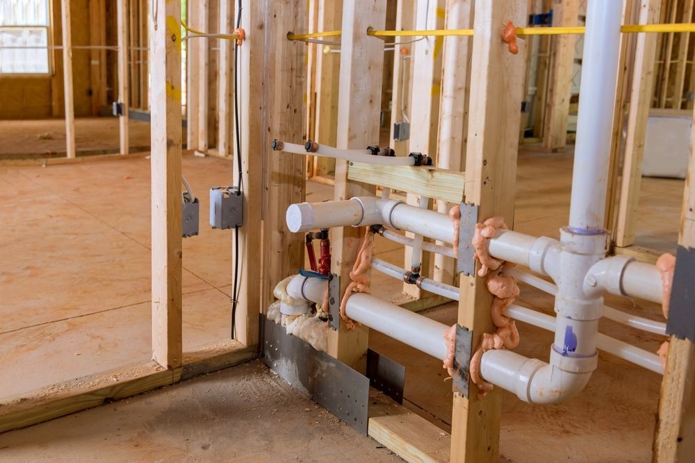 Interior view of a residential building under construction, featuring exposed wooden wall framing and white PVC plumbing.