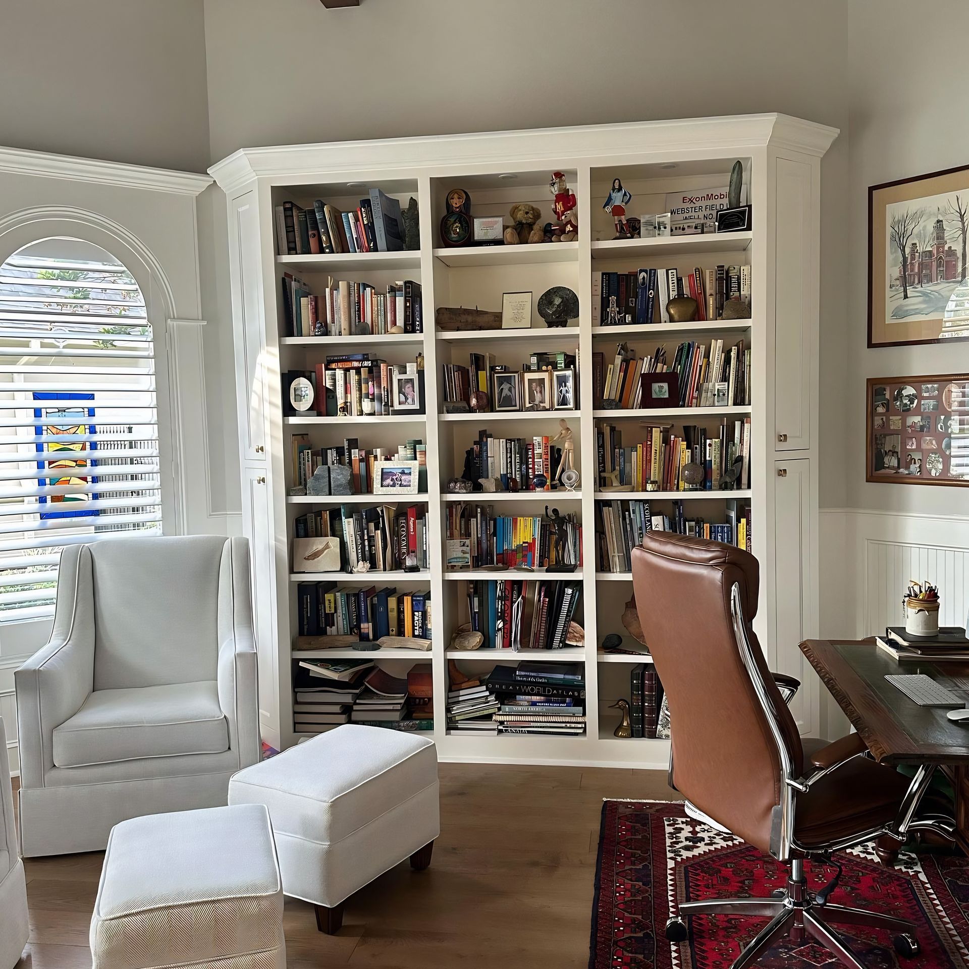 Bright living room with a white bookcase, armchair, ottoman, and desk on a red rug