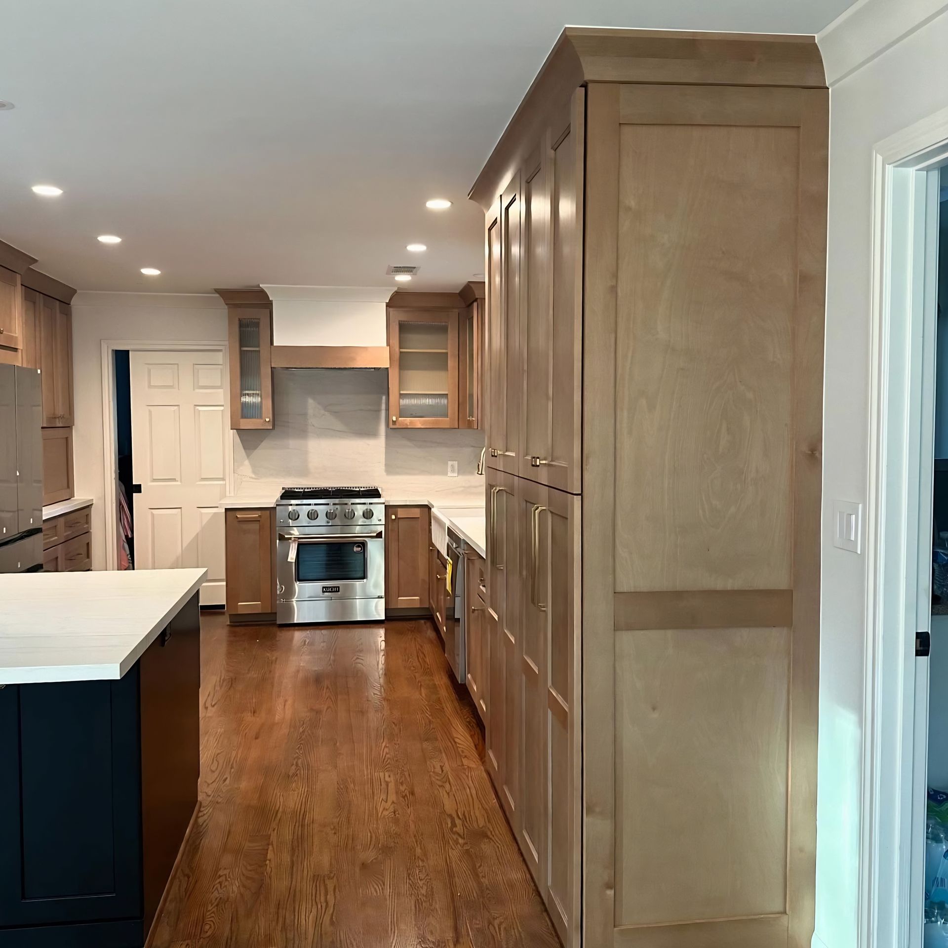Bright modern kitchen with wood floors, white cabinets, stainless steel stove, and a large pantry cabinet.