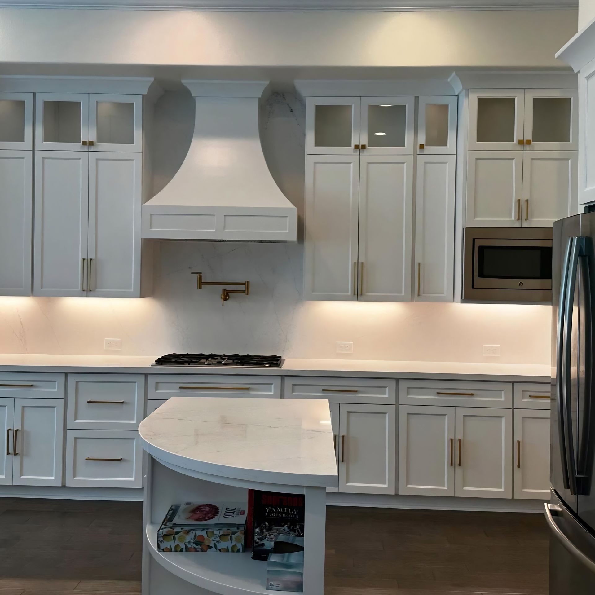 Bright white modern kitchen with cabinets, island, range hood, and stainless steel refrigerator