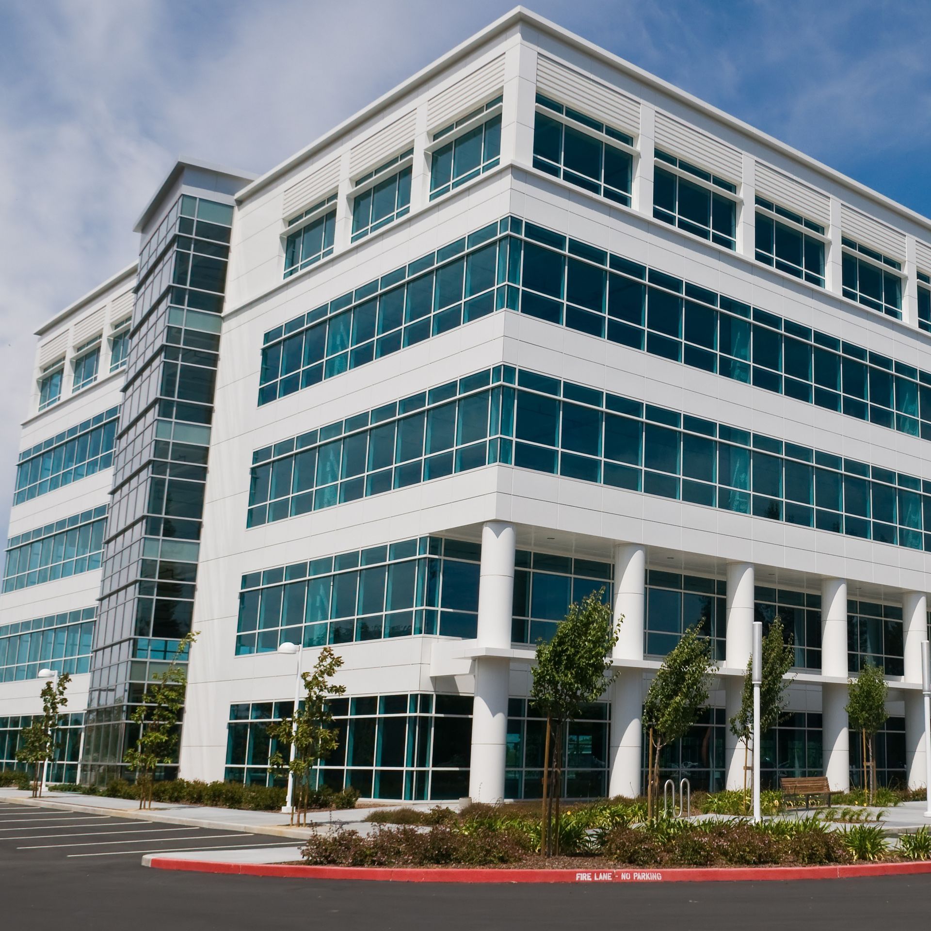 Modern glass office building with white trim and landscaped entrance under a blue sky