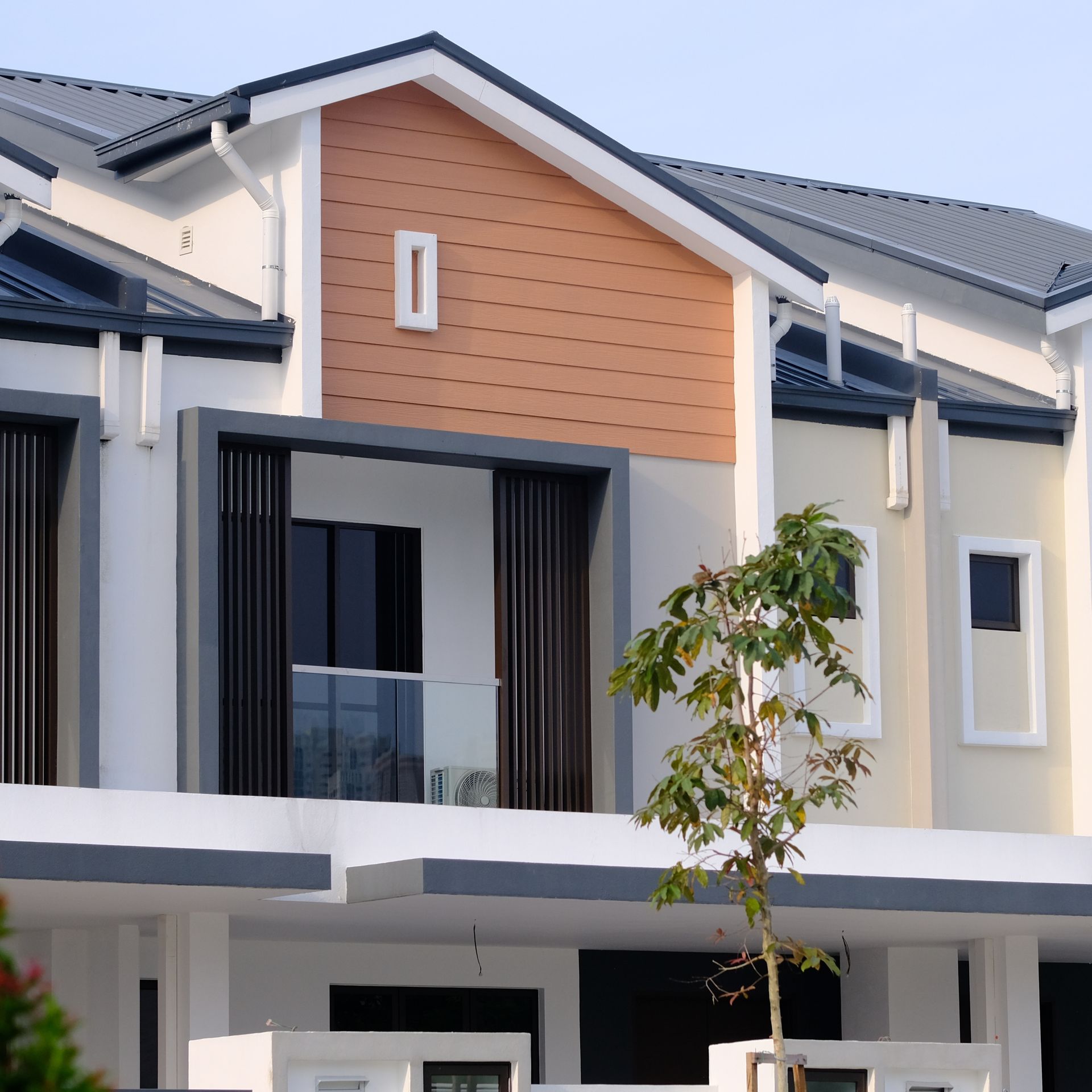 Modern townhouse exterior with white and gray walls, orange gable accent, and a small tree in front