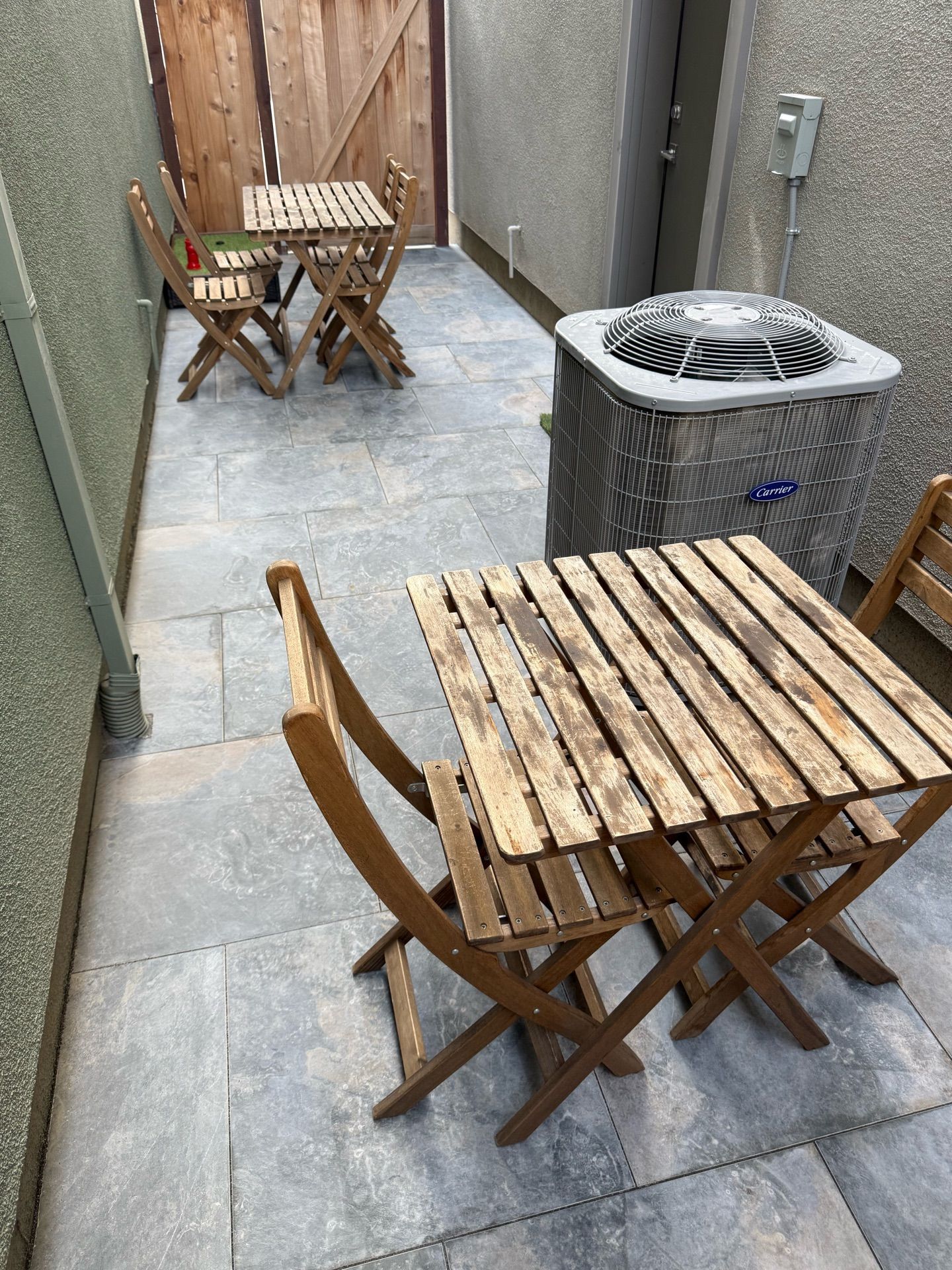 A wooden table and chairs are sitting on a patio next to an air conditioner.