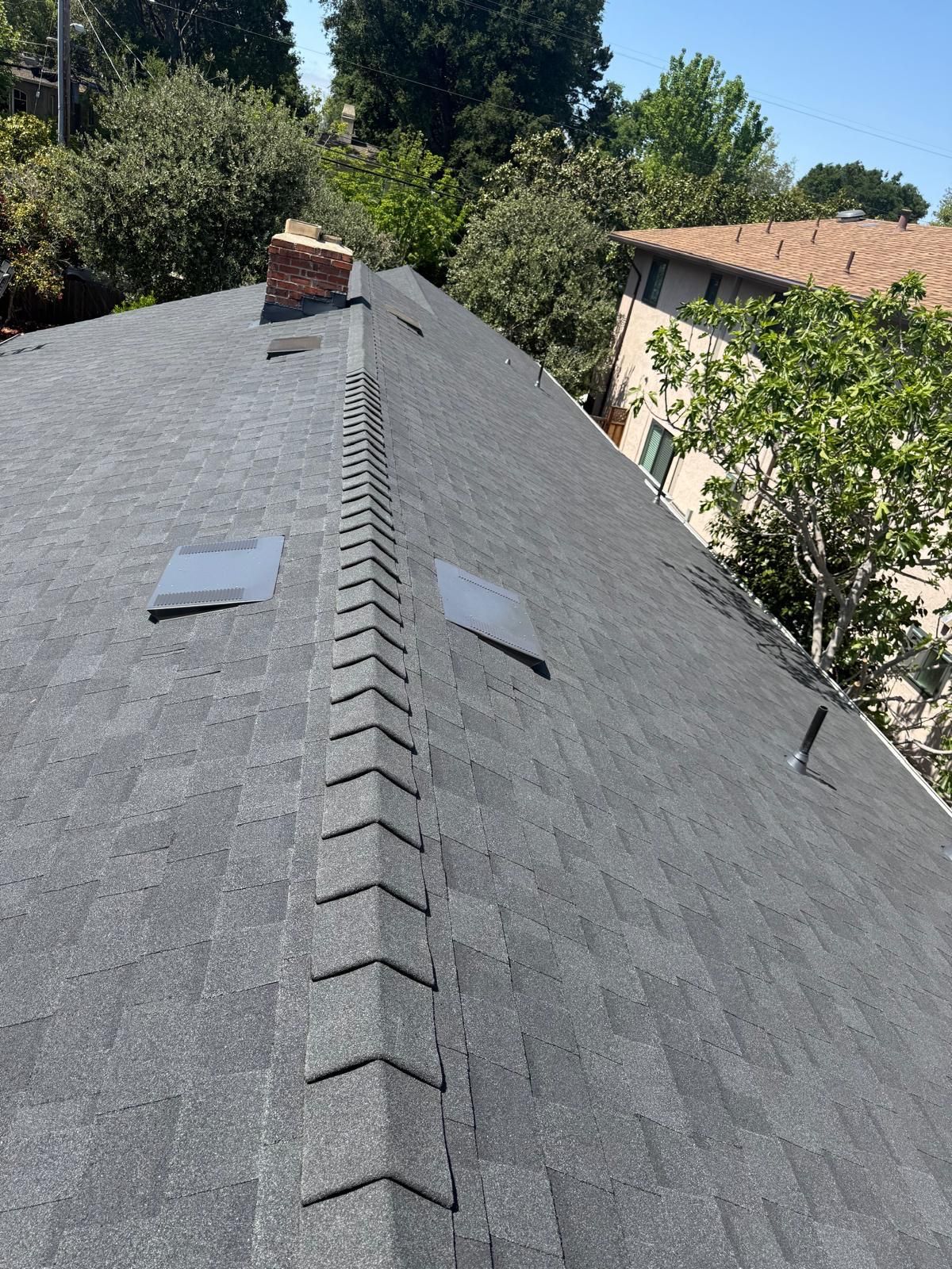 A close up of a roof with a chimney and trees in the background.