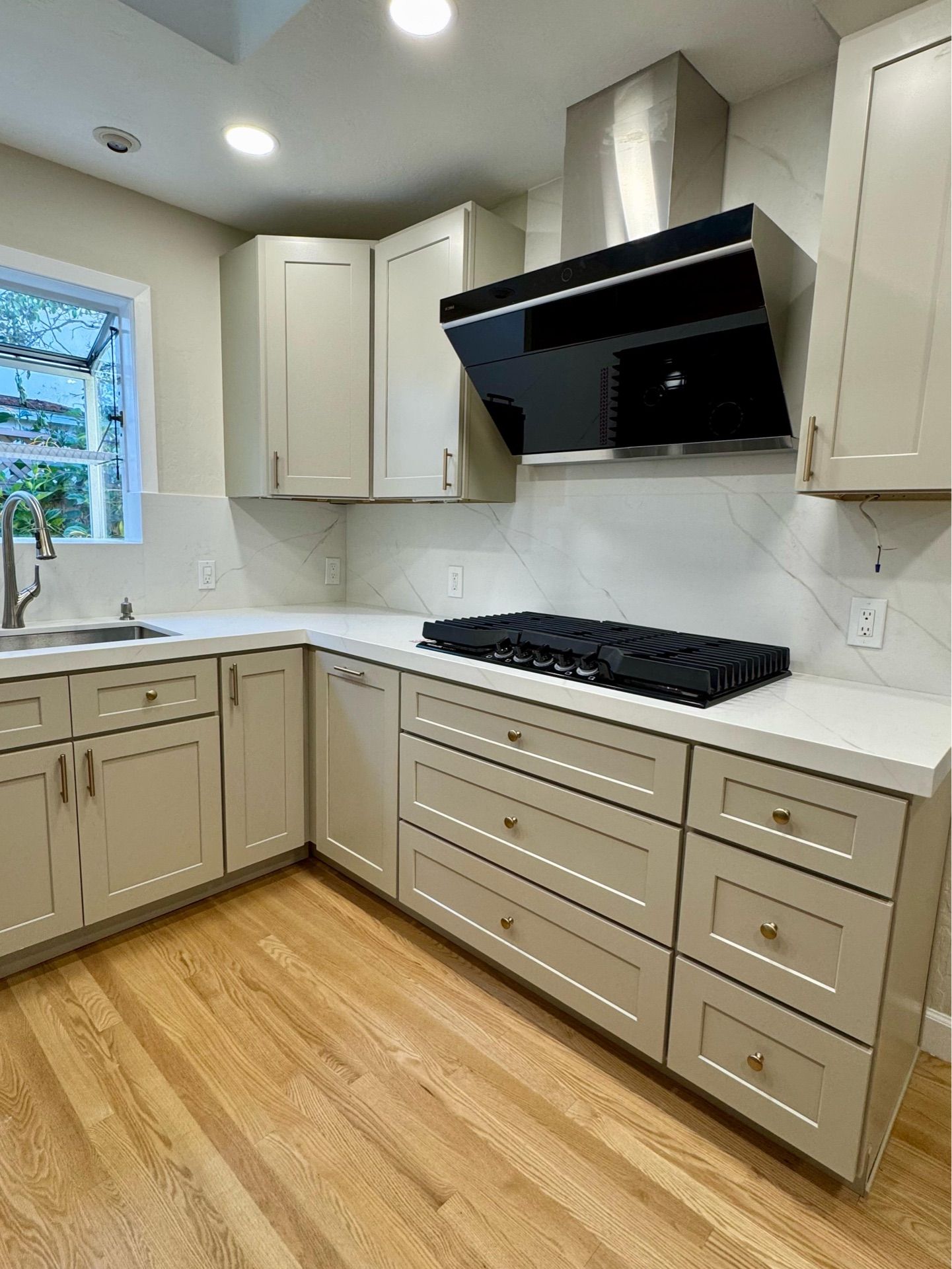 Modern kitchen with light wood floors, light gray cabinets, white countertops, and a black range hood.