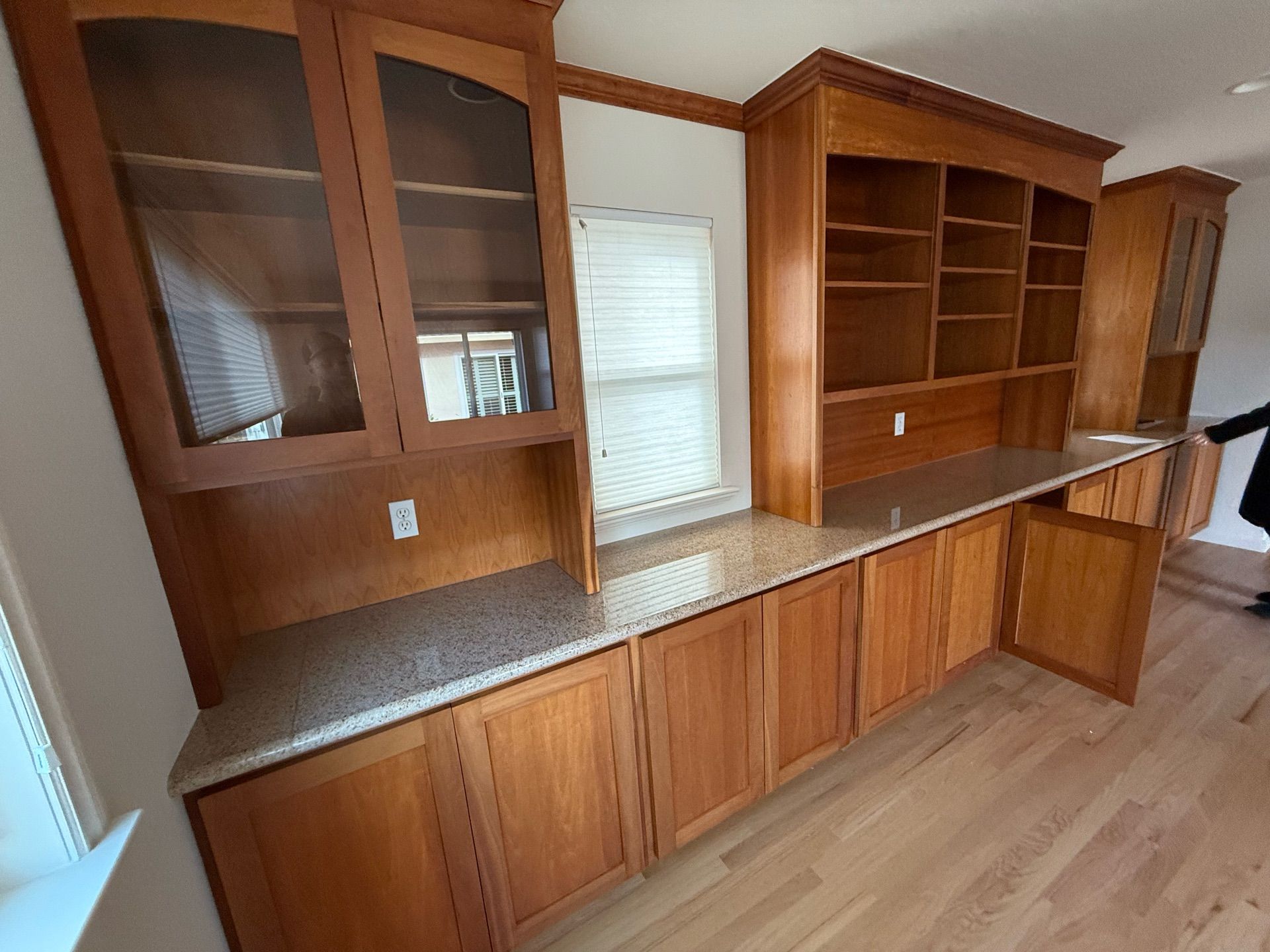 Built-in wooden cabinetry with a granite countertop, featuring glass-fronted cabinets and open shelving, spanning a wall.