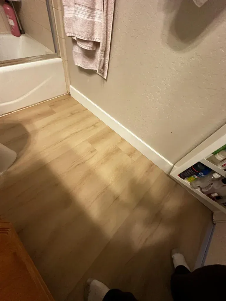 A person is standing in a bathroom with a wooden floor.