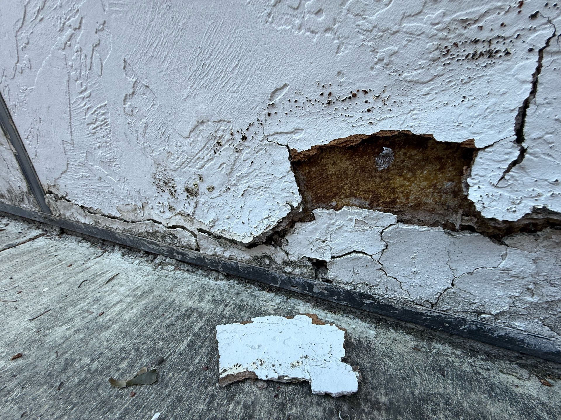 A piece of paper is laying on the ground next to a cracked wall.
