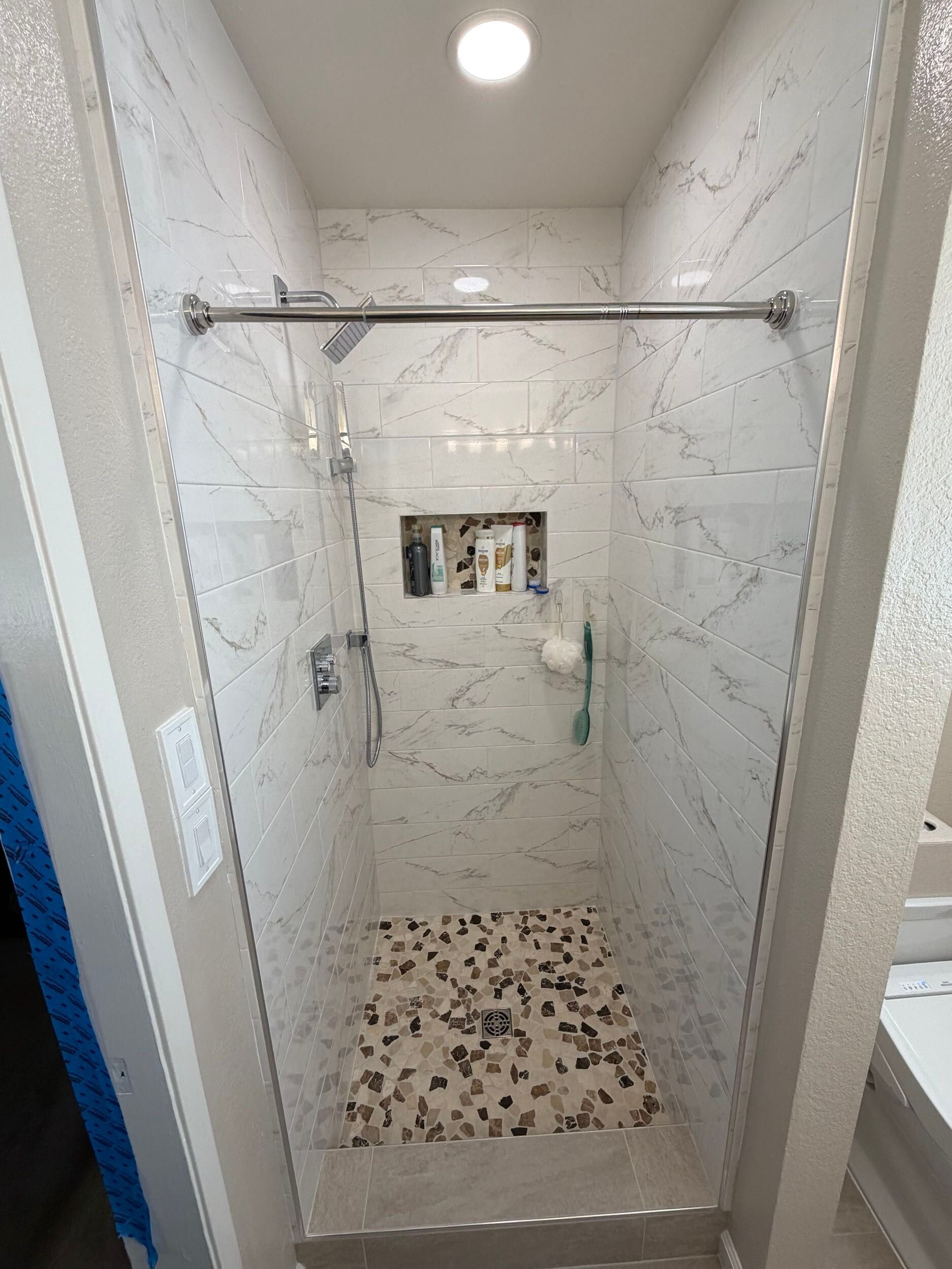 Updated bathroom remodel showcasing a modern walk-in shower with marble-style wall tile, pebble stone shower flooring, upgraded vanity with quartz countertop, contemporary sink and faucet, new lighting, and neutral color palette. Bathroom renovation completed by Dream Build Services, a residential remodeling contractor serving homeowners with bathroom and home renovation projects in the Bay Area.