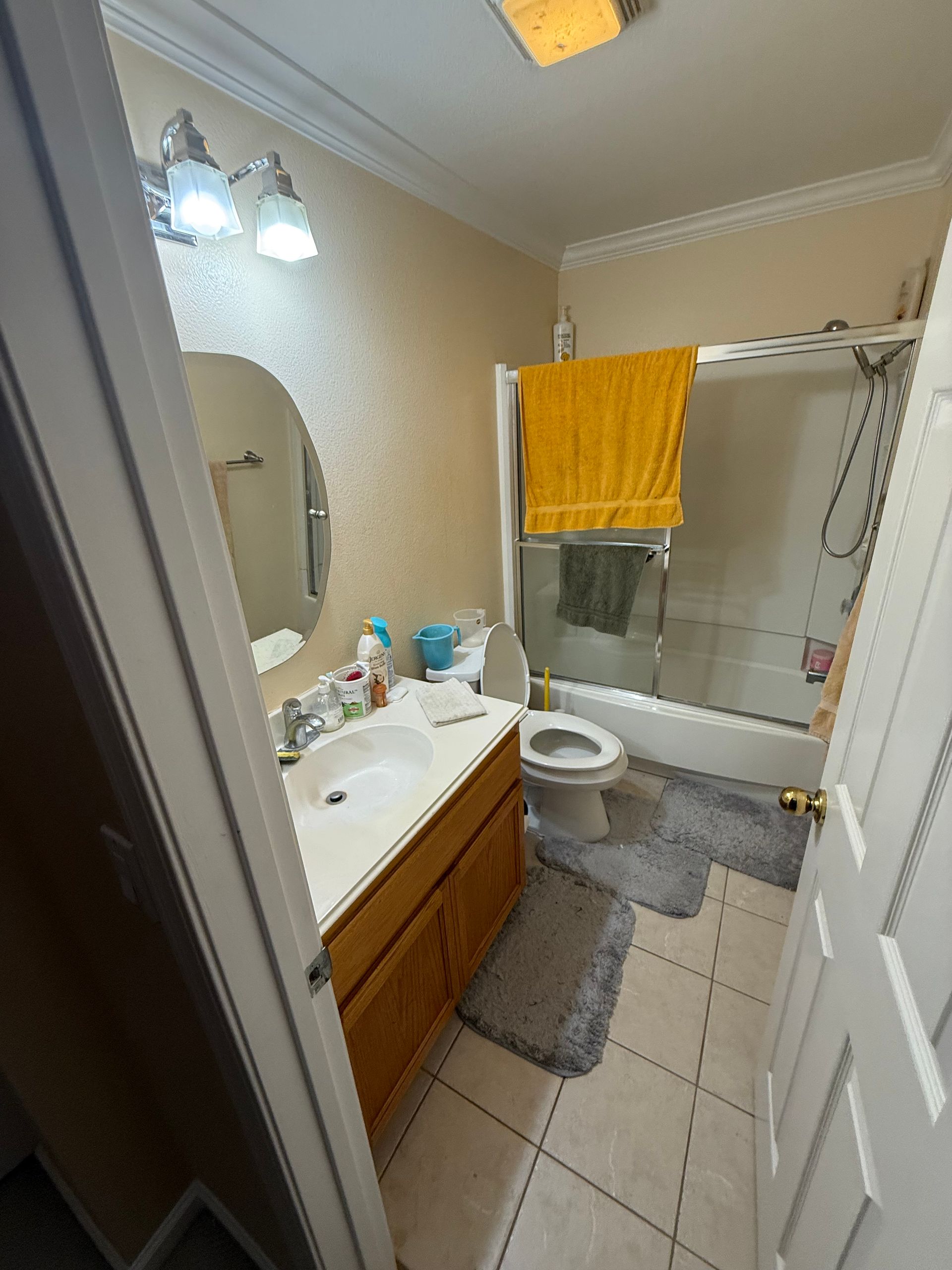 Small bathroom with white sink, toilet, tub, yellow towel, and gray tile floor.