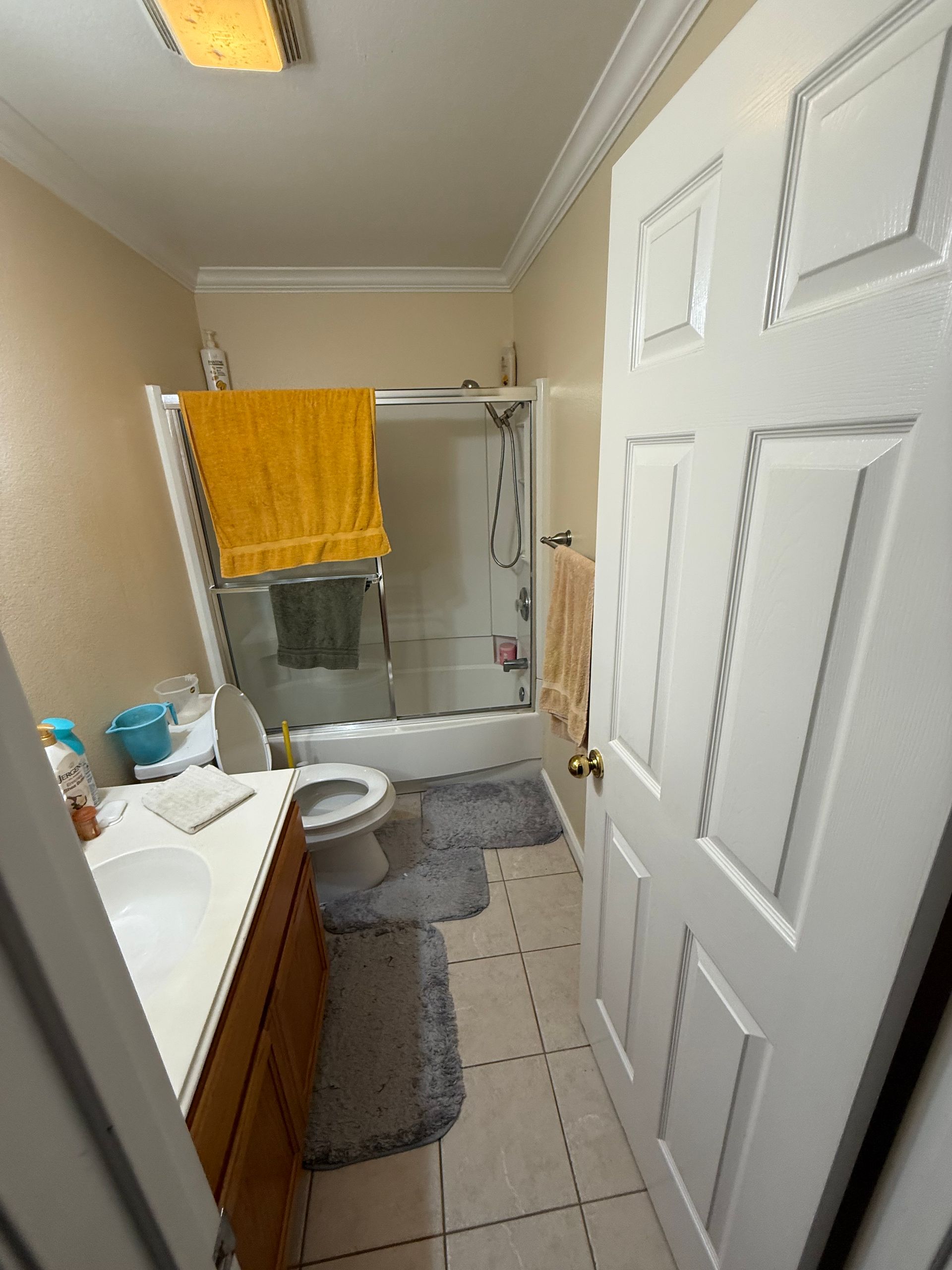 Small bathroom with shower curtain, toilet, sink, gray rugs, and a yellow towel on the shower rod.