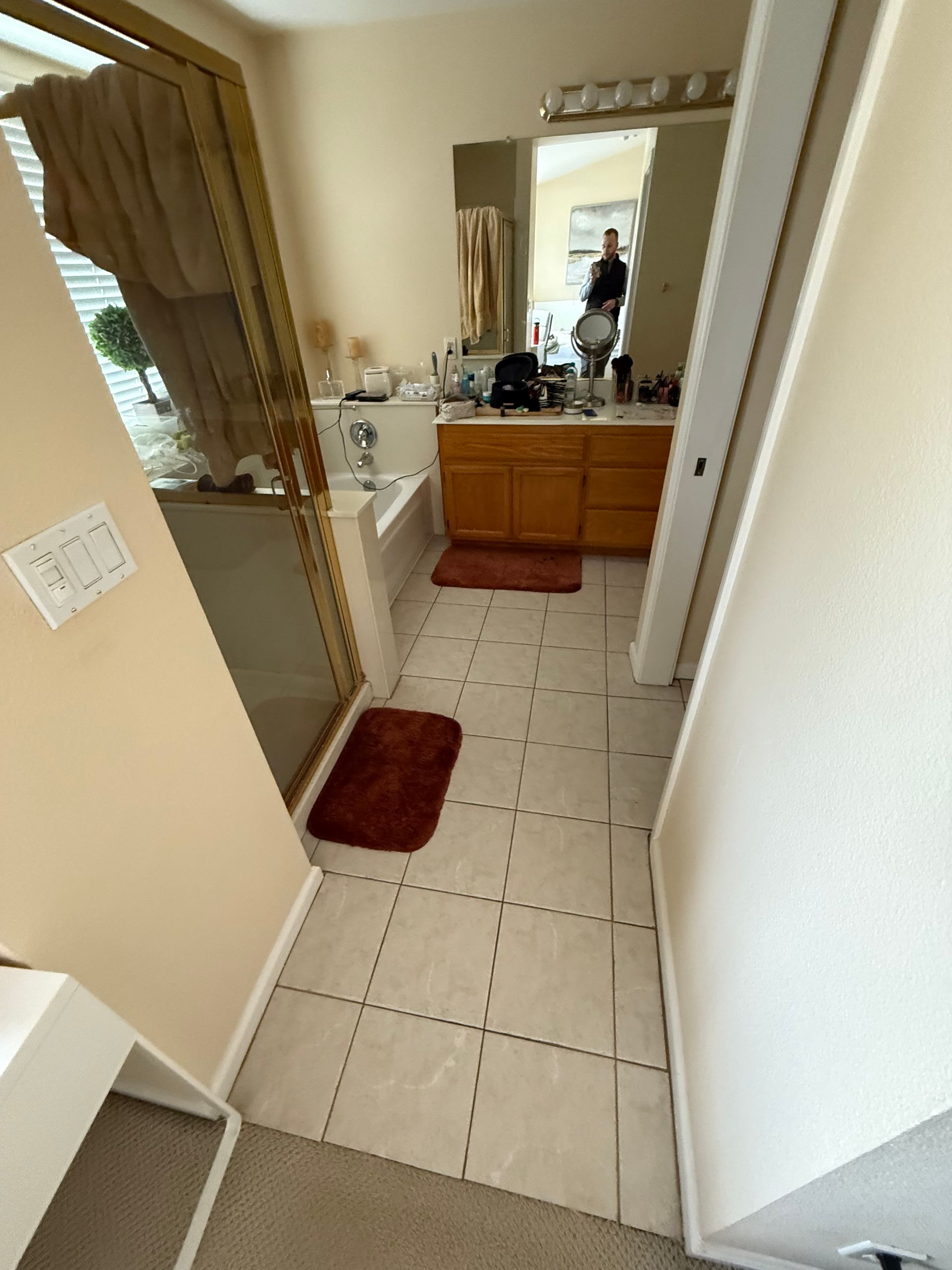 Narrow bathroom hallway with tiled floor, vanity mirror, beige walls, and a red rug near the sink.